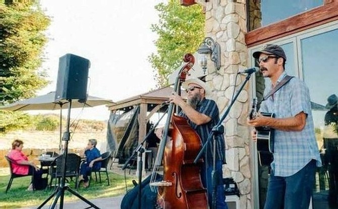 Two musicians playing guitar and string bass in front of the Calcareous wine tasting room for Wine Down Wednesday