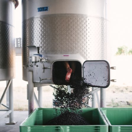 A stainless steel wine tank being cleaned out from the inside. Only a person's foot is visible through the opening at the bottom of the steel tank.